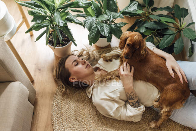 Giovane donna con Cocker Spaniel sdraiato sul tappeto a casa — Foto stock