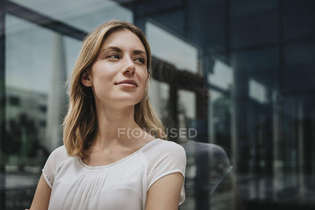 Blond woman looking away while day dreaming in front of glass wall — Stock Photo
