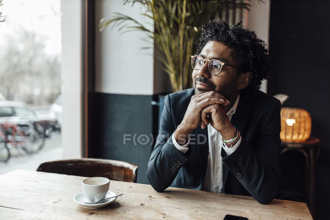 Думливий бізнесмен з рукою на підборіддя сидить у кафе, дивлячись на — стокове фото