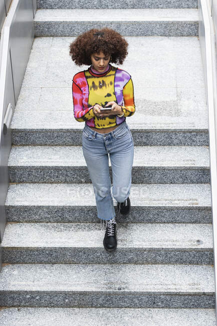 Jeune femme utilisant un téléphone portable tout en marchant sur l'escalier — Photo de stock