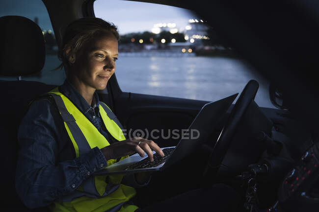 Professionista femminile utilizzando il computer portatile mentre seduto in auto al tramonto — Foto stock