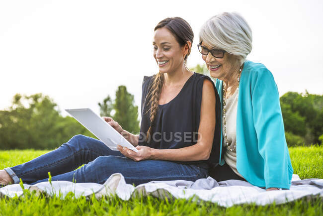 Nipote utilizzando tablet digitale mentre seduto con la nonna al parco — Foto stock