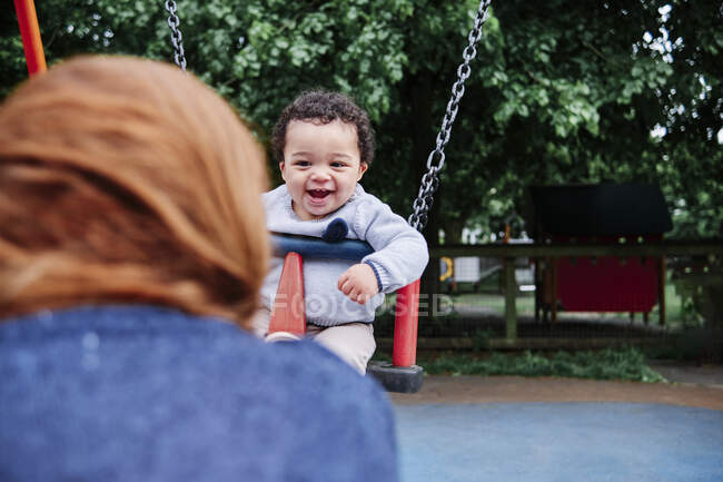 Lächelnder Junge schaukelt auf Spielplatz im Park — Stockfoto