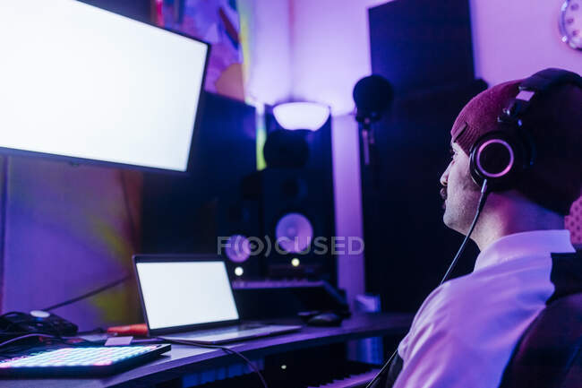 Mann mit Strickmütze schaut auf Bildschirm, während er im Studio Musik hört — Stockfoto