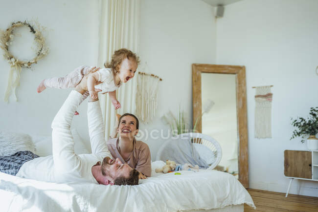Donna felice guardando figlia allegra raccolto da uomo sul letto a casa — Foto stock