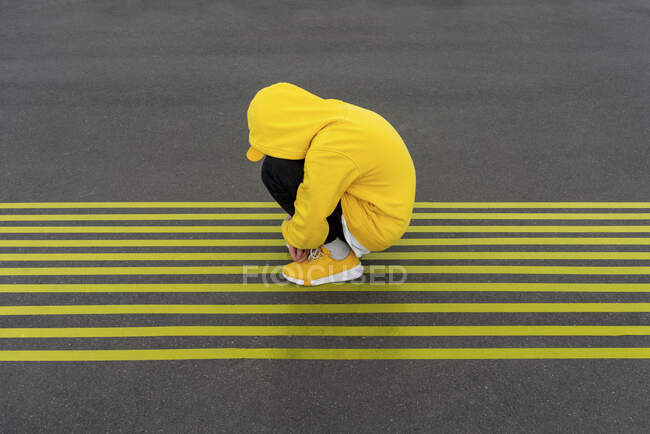 Rapaz deprimido agachado em marcas de estrada amarelas listradas — Fotografia de Stock