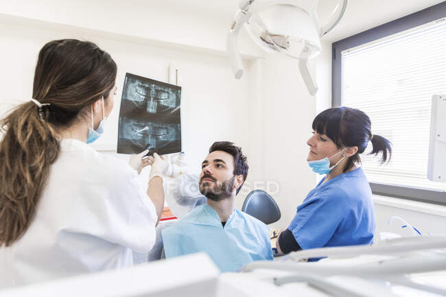 Dentiste avec assistante expliquant la radiographie au patient à la clinique médicale — Photo de stock