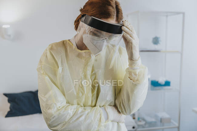 Trabajadora de la salud con ropa de trabajo protectora de pie con la mano en la sala de examen - foto de stock