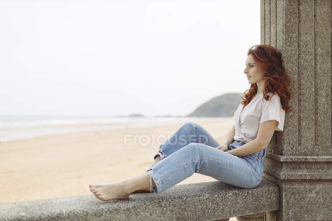 Rothaarige Frau sitzt tagsüber auf Stützmauer — Stockfoto