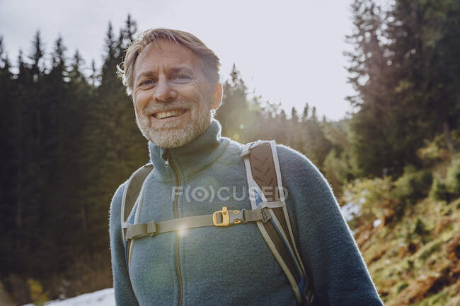 Homem bonito sorridente com mochila em pé na floresta contra o céu em Salzburger Land, Áustria — Fotografia de Stock