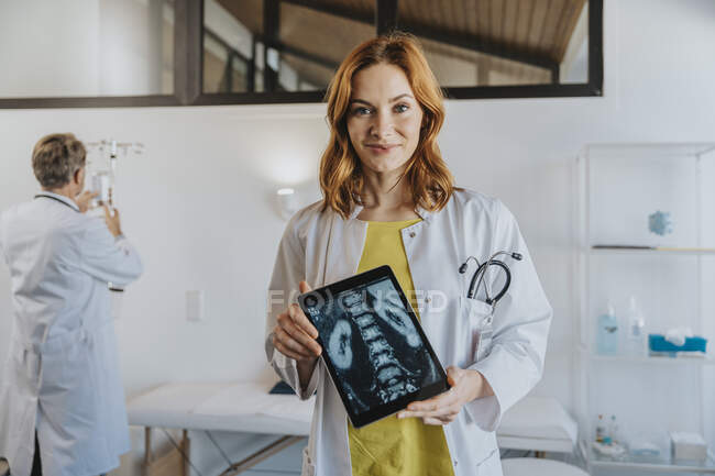Doctor showing x-ray image on digital tablet while standing with coworker in background at clinic — Stock Photo
