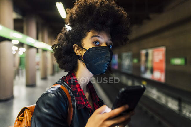 Jovem com máscara protetora segurando telefone celular no metrô — Fotografia de Stock