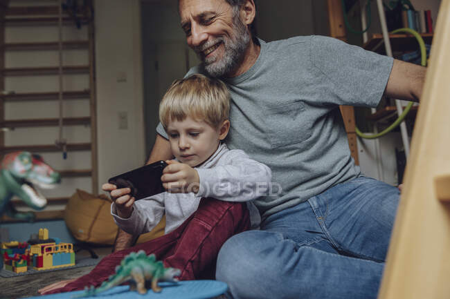 Padre guardando il figlio giocare su smart phone a casa — Foto stock