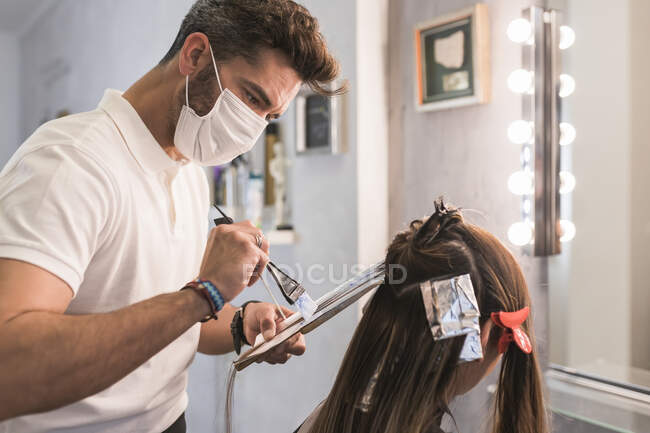 Чоловічий перукар з захисною маскою для обличчя фарбує волосся клієнта в салоні — стокове фото