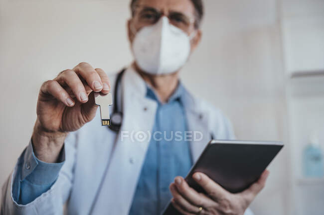 Doctor holding USB stick and digital tablet while standing in clinic — Stock Photo
