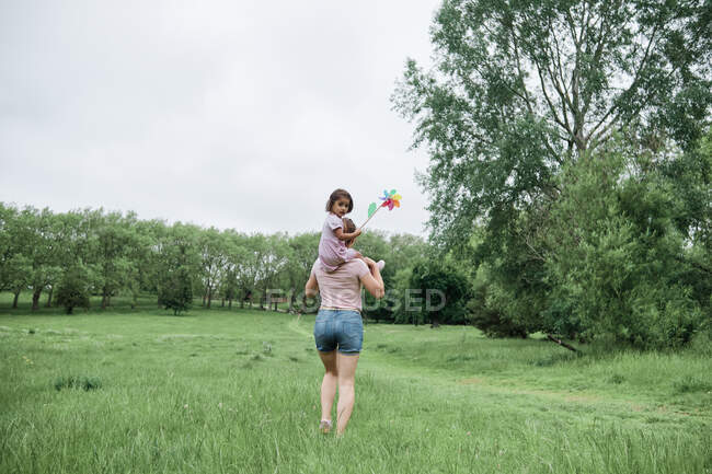 Madre che porta la figlia sulle spalle mentre cammina nel parco — Foto stock