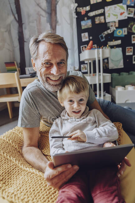 Усміхаючись батько і син з цифровим планшетом у спальні. — стокове фото