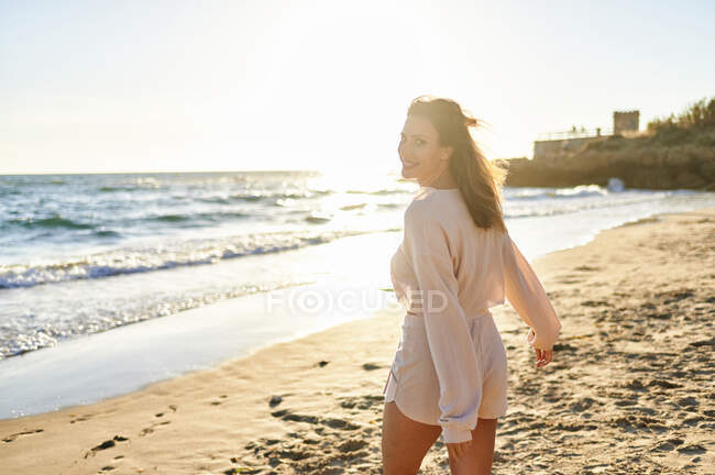 Donna sorridente che guarda oltre le spalle mentre cammina in spiaggia — Foto stock