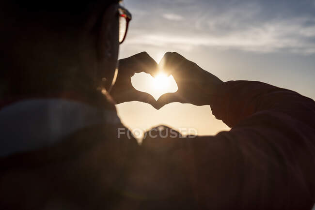 Femme faisant forme de coeur avec les mains pendant le coucher du soleil — Photo de stock