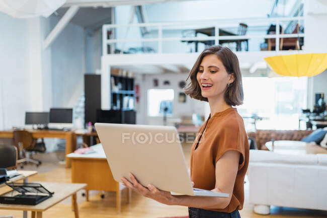 Felice professionista femminile utilizzando il computer portatile mentre in piedi in ufficio creativo — Foto stock