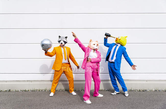 Tre persone che indossano abiti vibranti e maschere animali che festeggiano davanti al muro bianco — Foto stock