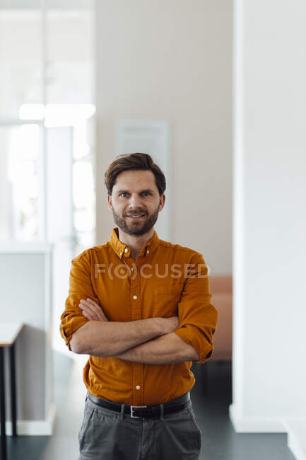 Homme d'affaires souriant les bras croisés debout dans le bureau — Photo de stock