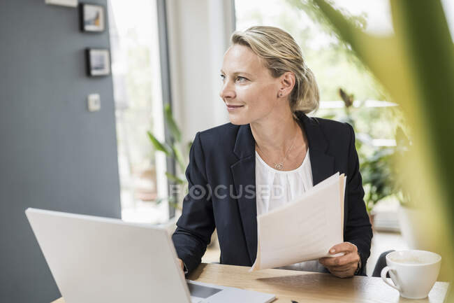 Mujer de negocios reflexiva con documento y portátil en la oficina - foto de stock