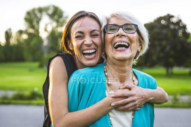 Веселая внучка обнимает бабушку сзади в парке — стоковое фото