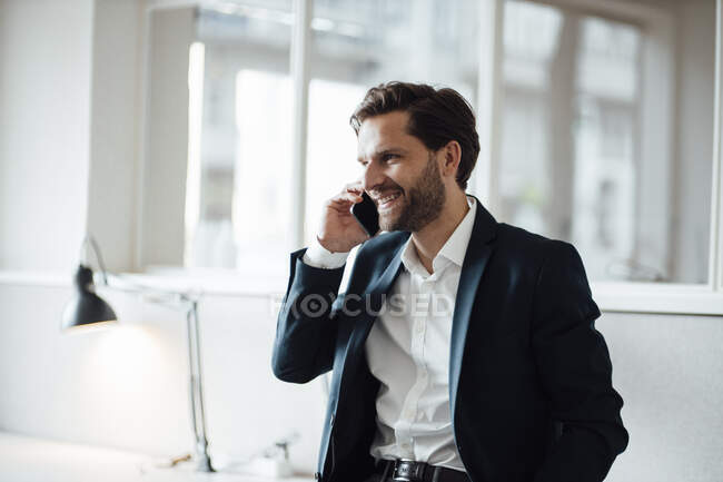 Усміхнений бізнесмен розмовляє по телефону в офісі — стокове фото
