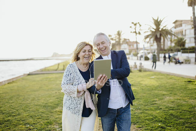Счастливая зрелая пара делится цифровым планшетом во время просмотра видео во время отпуска — стоковое фото