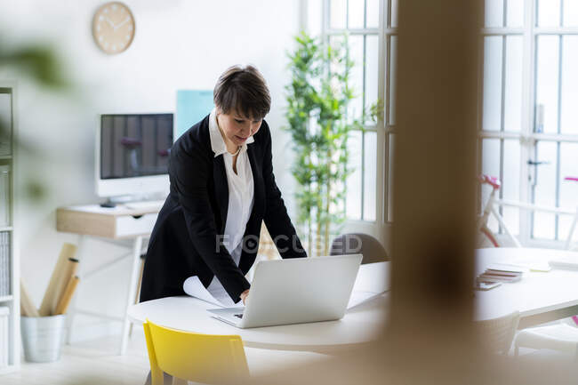 Businesswoman using laptop while standing at desk in office — Stock Photo