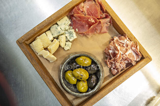 Зеленая и черная оливка подается с красным мясом и сыром в деревянном подносе — стоковое фото