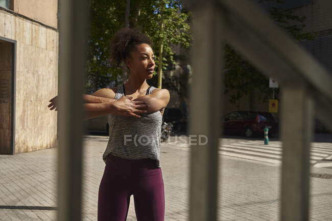 Sportswoman étirement le jour ensoleillé vu à travers la clôture — Photo de stock