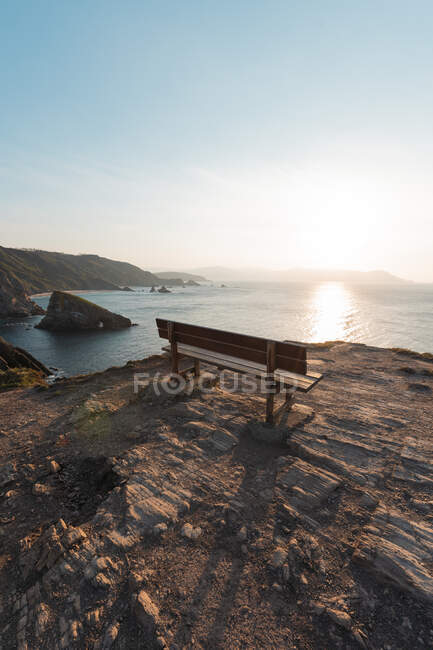 Пустая скамейка, стоящая на краю прибрежной скалы на закате — стоковое фото