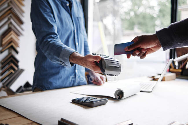 Виробник кадрів тримає читача кредитних карток, поки клієнт платить у майстерні — стокове фото