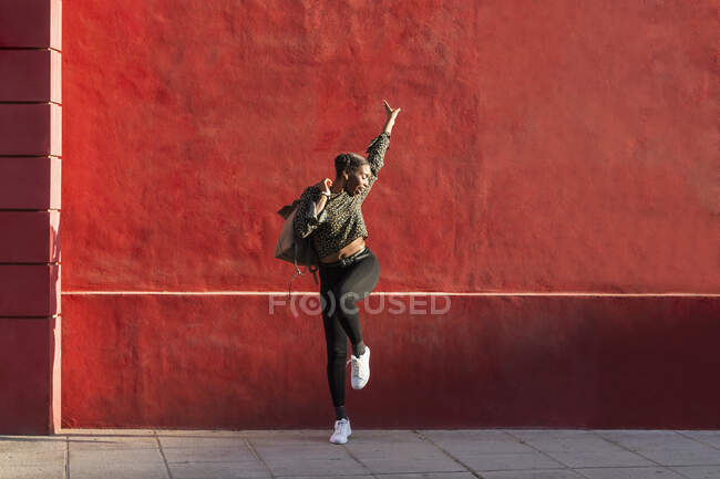 Mulher despreocupada de pé com a mão levantada em pé na frente da parede — Fotografia de Stock