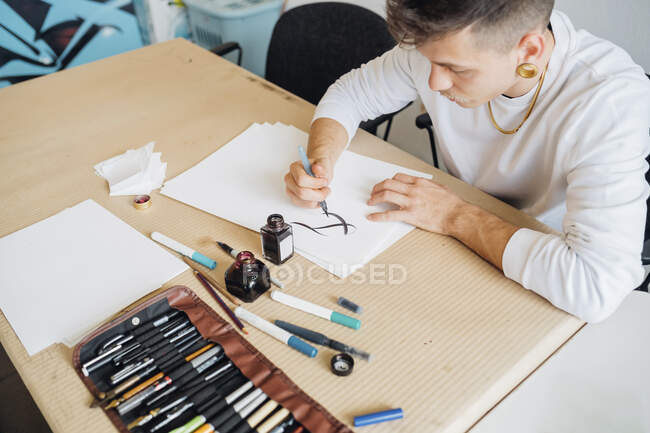 Hipster young man practicing calligraphy on paper in studio — Stock Photo