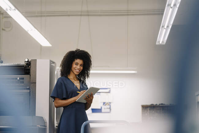 Smiling Afro female entrepreneur looking away while working on digital tablet at industry — Stock Photo