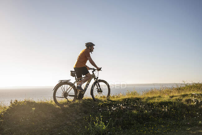 Чоловік спортсмен їде на електричному гірському велосипеді на зеленій траві на заході сонця — стокове фото
