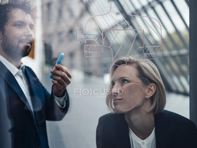 Gelangweilte Geschäftsfrau lehnt an Glaswand, während Geschäftsmann im Büro über Diagramm diskutiert — Stockfoto