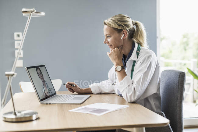 Жіночий лікар розмовляє з колегою через відеодзвінок на ноутбуці в офісі — стокове фото