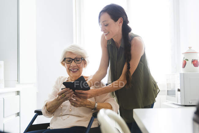 Donna sorridente che insegna alla nonna disabile usando lo smartphone a casa — Foto stock