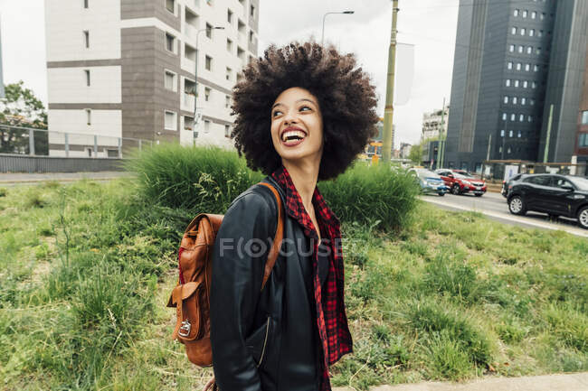 Mujer feliz con mochila mirando hacia atrás por encima del hombro en la ciudad - foto de stock