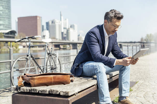 Чоловік - підприємець використовує цифрову табличку, сидячи на лавці. — стокове фото