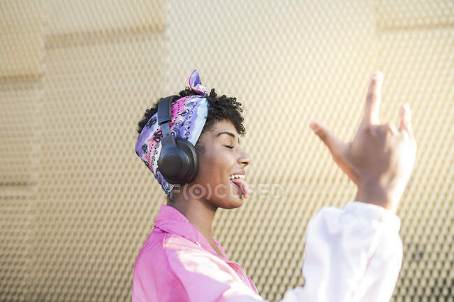 Обережна жінка робить знак рогу, слухаючи музику на навушниках. — стокове фото