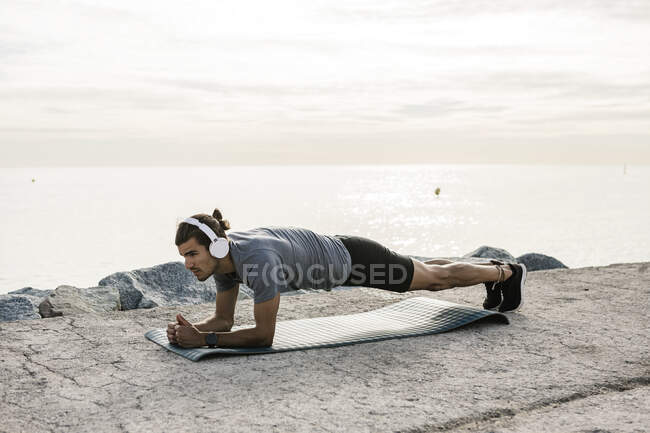 Männlicher Athlet mit Kopfhörer übt Plankenstellung auf Trainingsmatte — Stockfoto