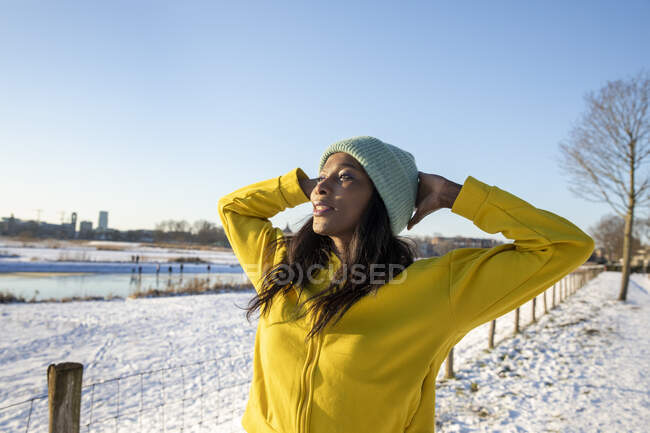 Woman wearing knit hat standing with hands behind head while looking away — Stock Photo