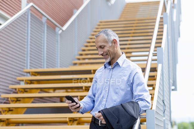 Uomo d'affari che utilizza lo smartphone mentre si appoggia sulla ringhiera vicino a passi — Foto stock
