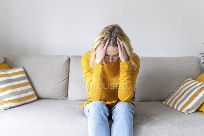 Женщина с головой в руках сидит дома на диване — стоковое фото