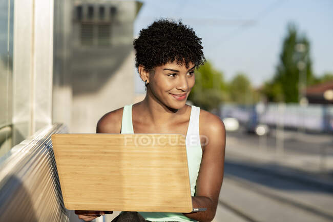Молодая женщина смотрит в сторону, держа ноутбук — стоковое фото